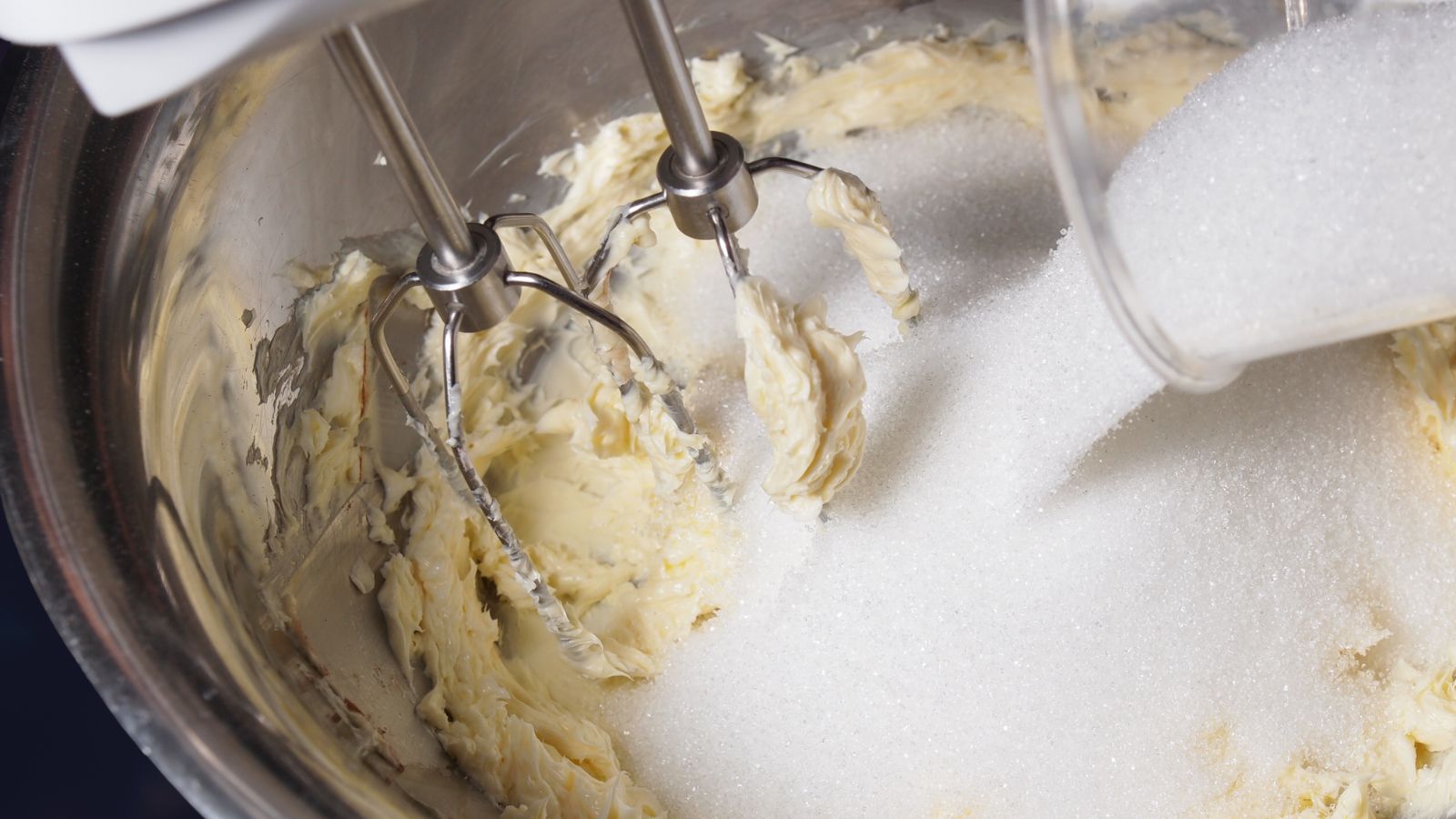 Ginger biscuit recipe image of a metal mixing bowl with sugar and butter being mixed together