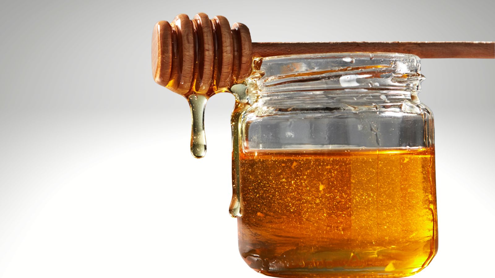 kitchen cupboard staples, honey image of honey in a jar with a honey stick on the top on a gradient grey background