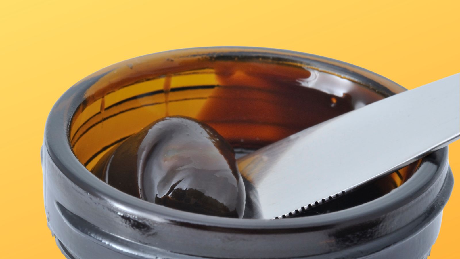 Kitchen cupboard staples, image of a pot of marmite on a yellow background with a knife digging some marmite out of the jar
