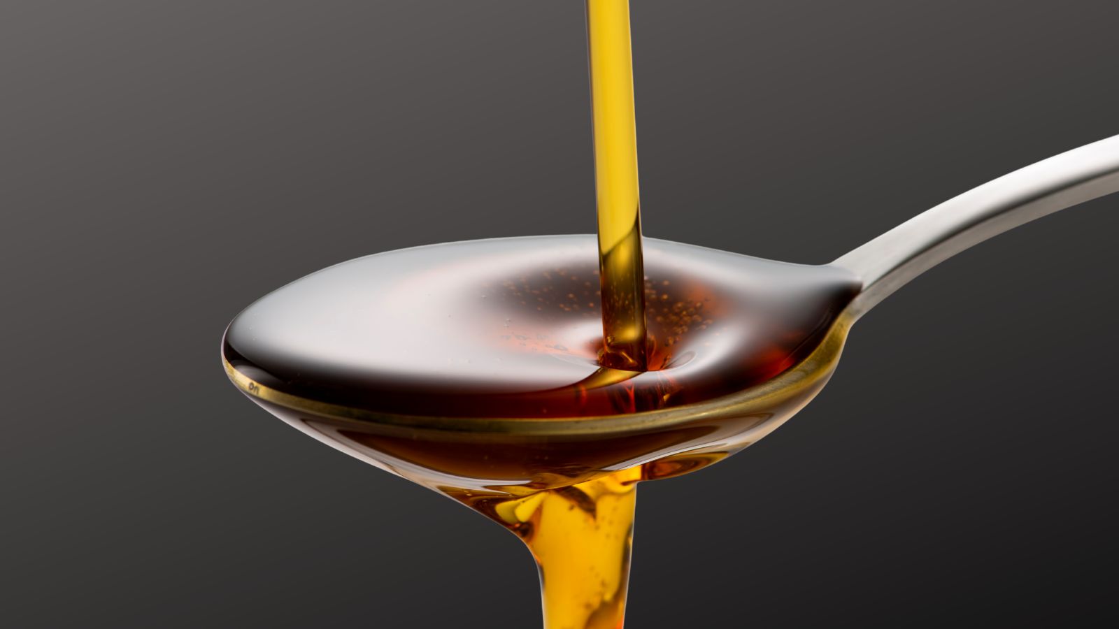 Kitchen cupboard staples toasted sesame oil image of a spoon of toasted sesame oil on grey background