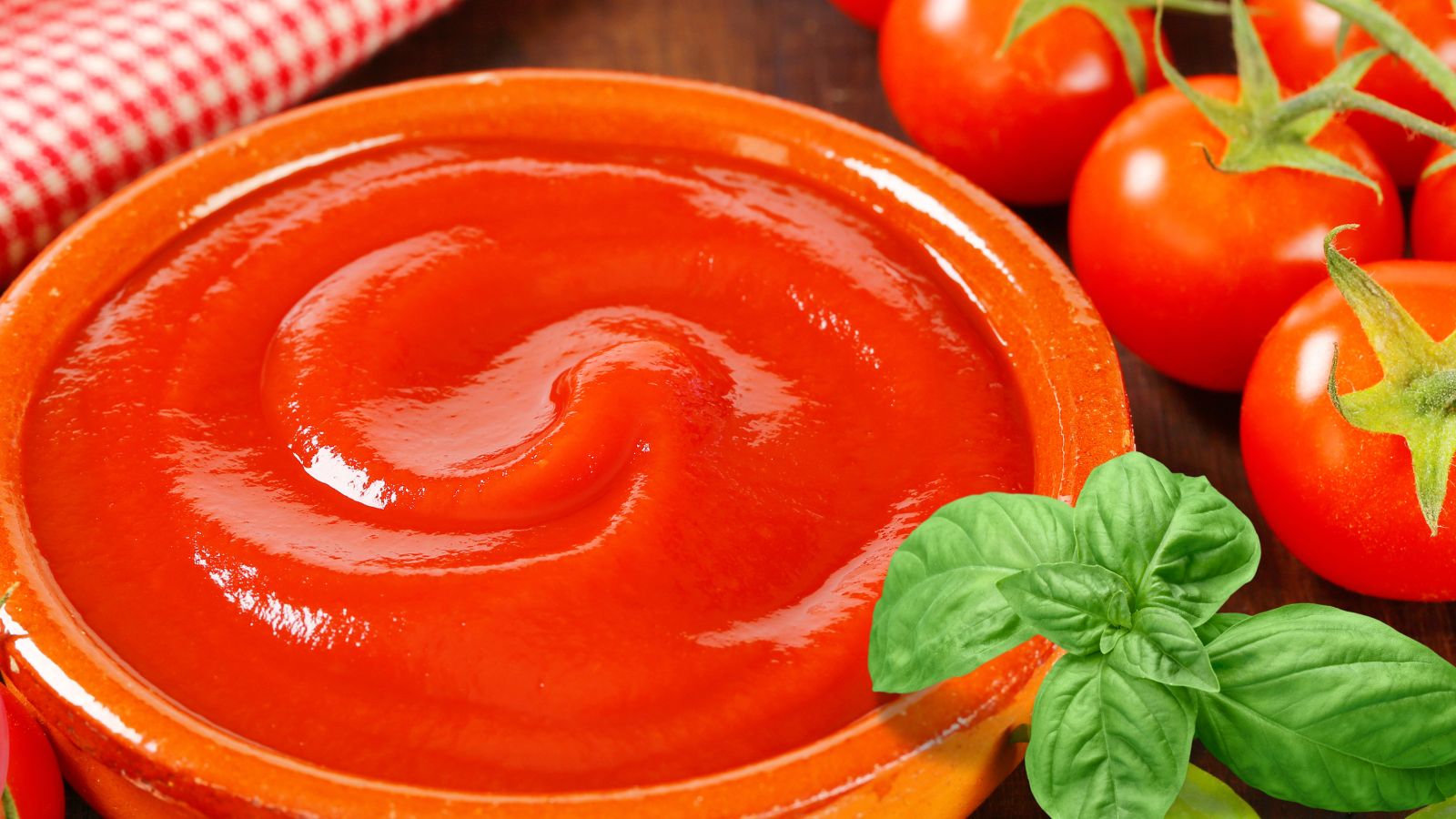 Kitchen cupboard staples image of tomato passata and basil in a bowl with vine ripened tomatoes in background