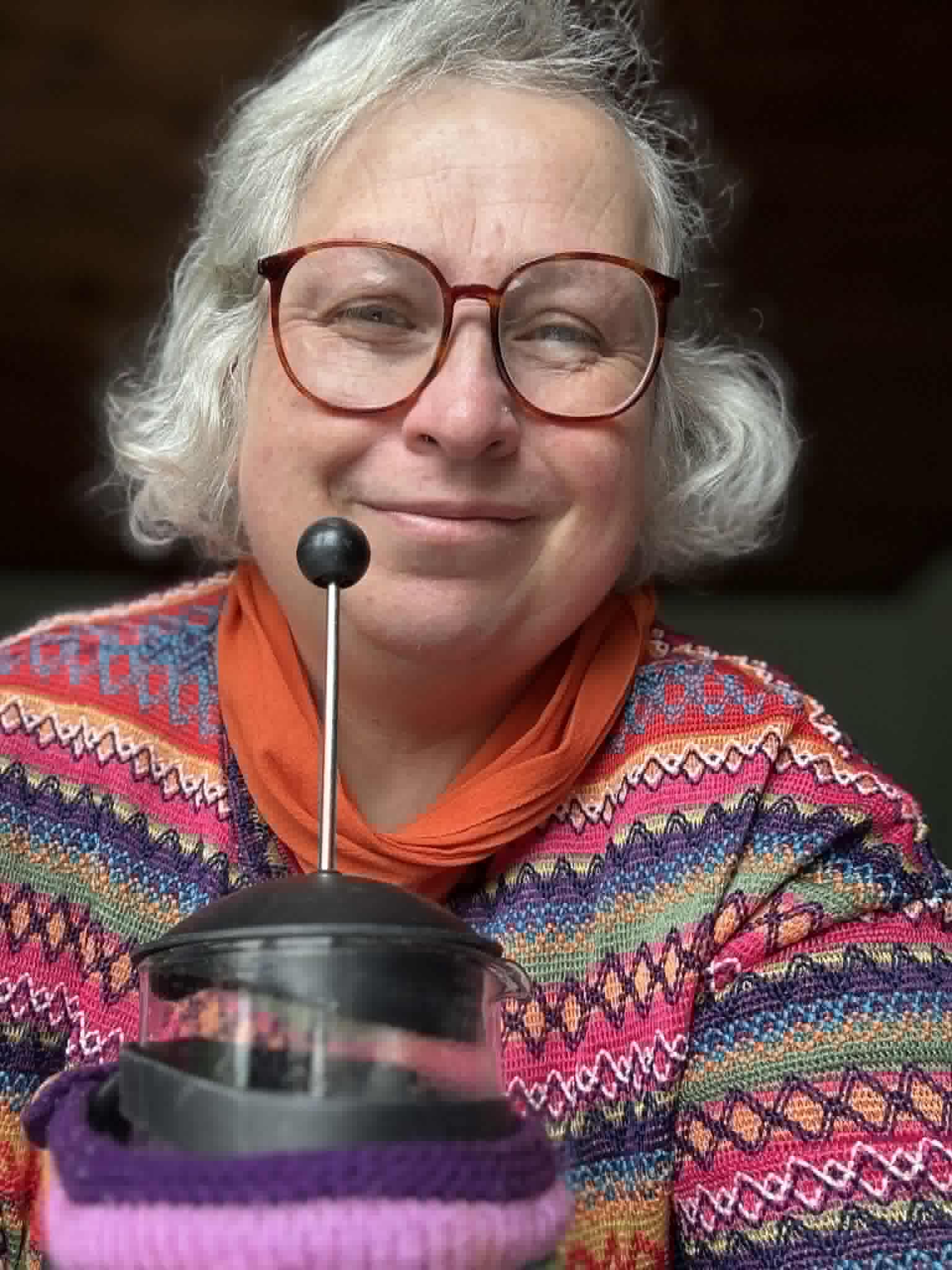 image of Mama Coops aka Sarah Cooper in a brightly coloured rainbow jumper, carrying a cafeitiere of coffee