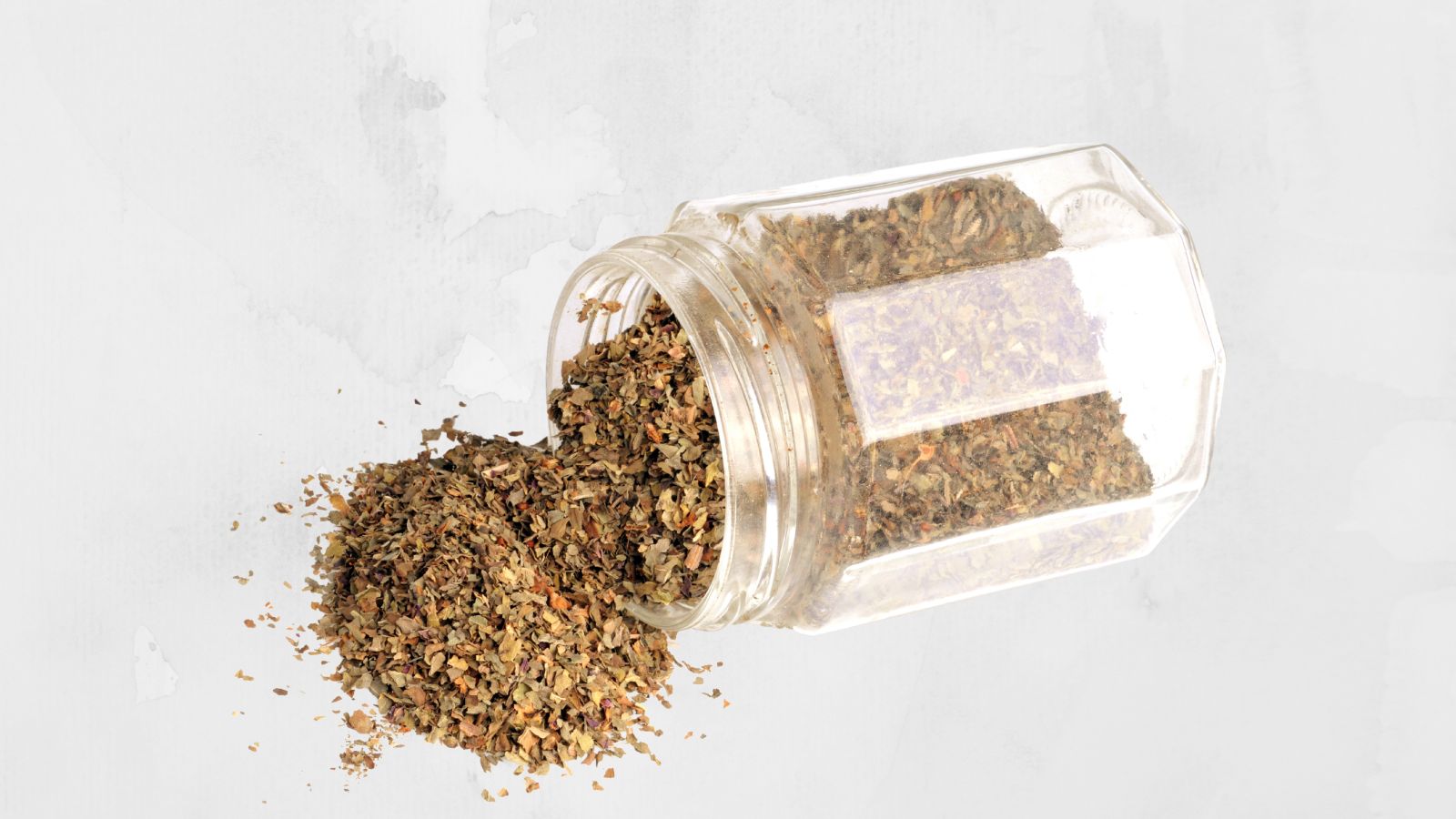 spice rack, image of a pot of dried basil lying on its side with basil spilling out onto the worktop